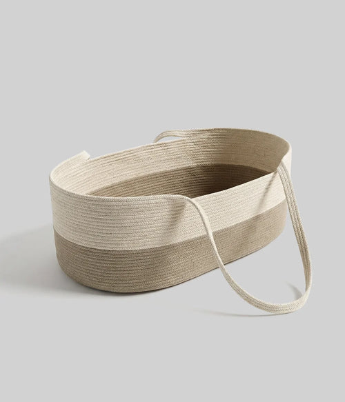 The Baby Rest Basket is a two-tone oval woven basket in beige and light brown with handles, made from natural cotton. Stylish and perfect as a مهد حديثي الولادة, it’s shown on a light gray background.