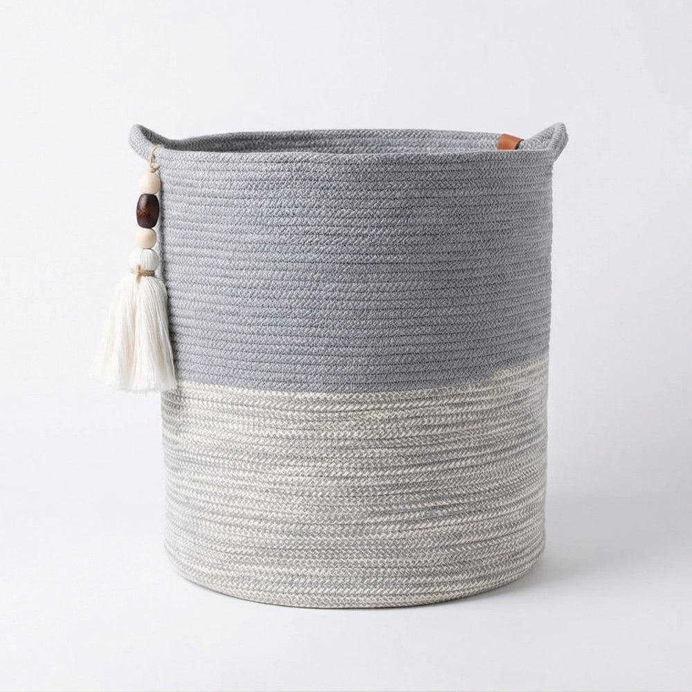 The Ocean Gray Basket is a round woven باسكت يدوي قطني with two handles, featuring a light gray bottom and dark gray top. A decorative tassel with beads hangs from one handle. This باسكت ديكور is displayed on a plain white background.