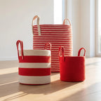 Three Terra Red Baskets—woven with red and white stripes and solid red designs—feature sturdy handles. Each sits on a wooden floor in sunlight, perfect for organizing or as a blanket storage basket (باسكت لتخزين البطاطين).