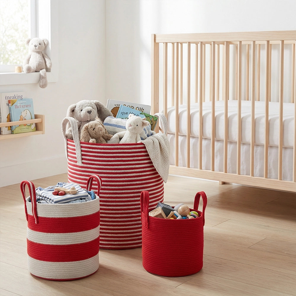 Three Terra Red Baskets filled with toys and books sit on a wooden floor near a light wood crib and window in a bright, tidy nursery. A stuffed bear rests on the windowsill.