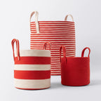 Three Terra Red Baskets with handles, featuring red and white stripes and solid red designs, are shown against a plain background. Available in different sizes, they’re perfect for storing blankets or organizing your space.